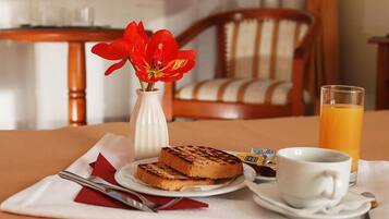 A breakfast setting with toast, a cup of coffee, a glass of orange juice, and a vase with red flowers on a table.