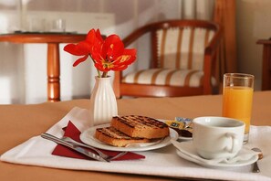 A breakfast setting with toast, a cup of coffee, a glass of orange juice, and a vase with red flowers on a table. - Hotel Moldova (Iasi)