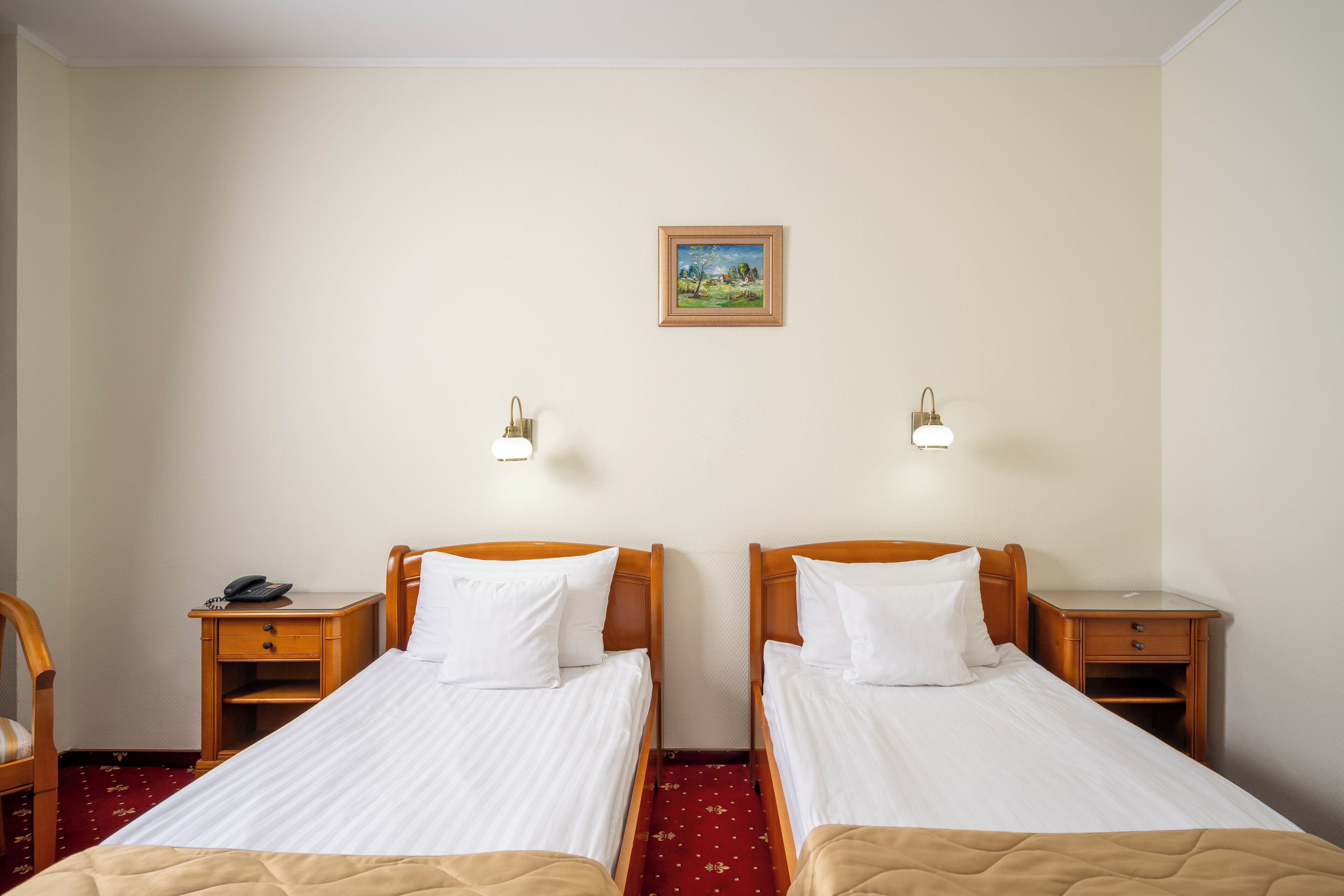 A hotel room with two single beds, bedside tables with lamps, a small desk, and a chair.