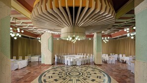 A banquet hall with a central round table surrounded by white tables, chandeliers, and a patterned floor. - Hotel Moldova (Iasi)