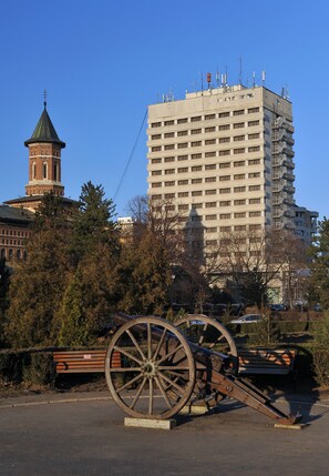 A historic building with a clock tower, a modern high-rise building, and a park with a wooden bench and a large wheel. - Hotel Moldova (Iasi)