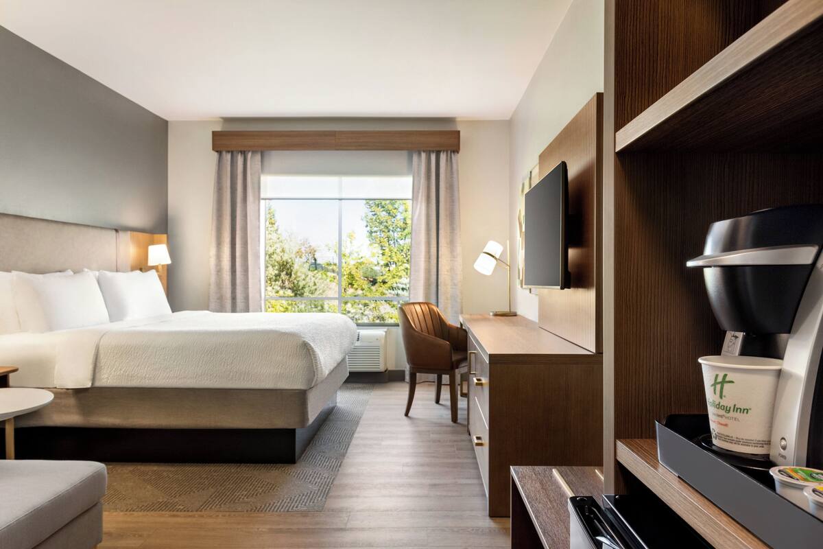 A hotel room with a bed, desk, chair, TV, and coffee machine.