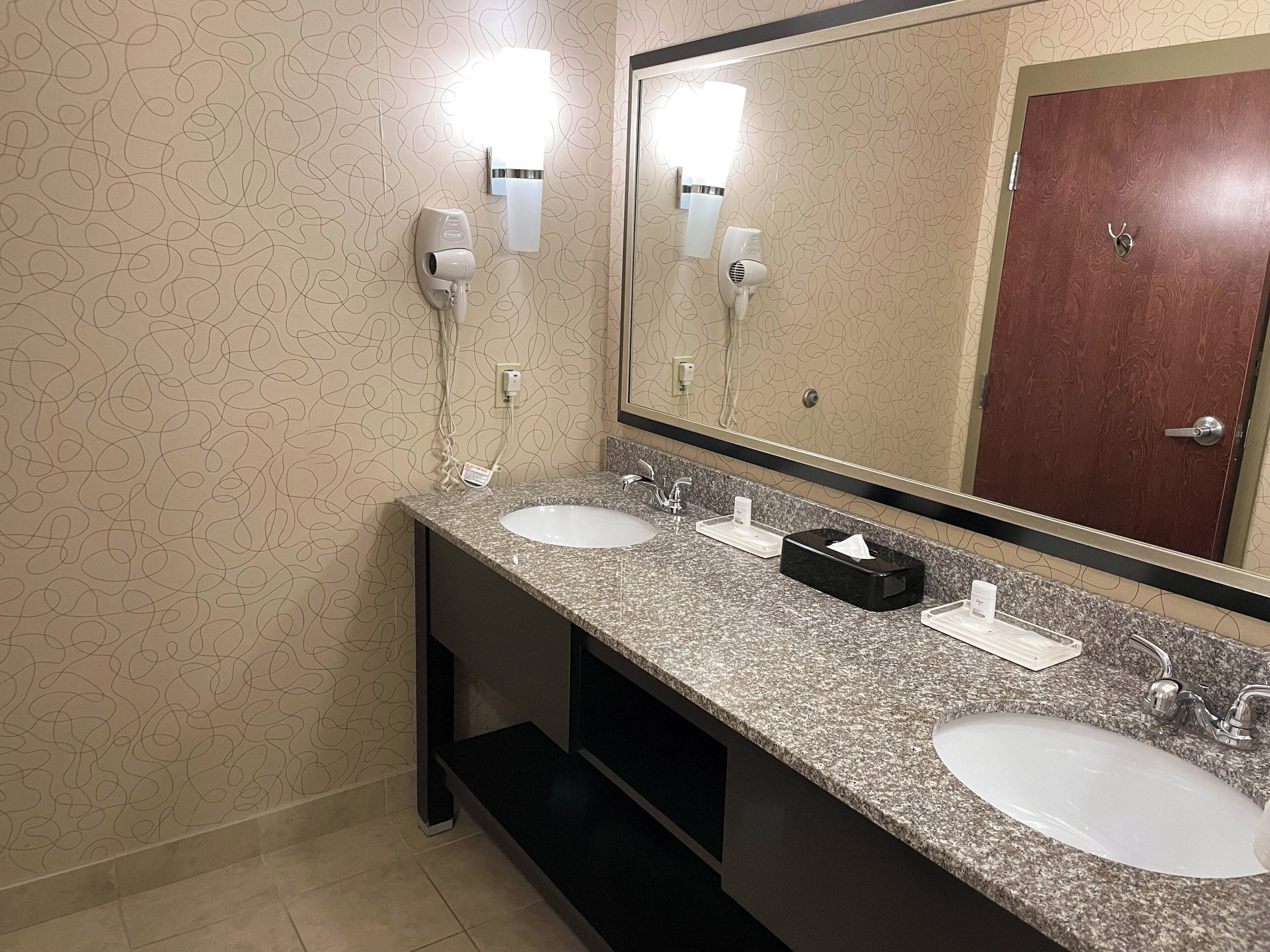 Un baño con dos lavamanos, un espejo grande y un dispensador de toallas.