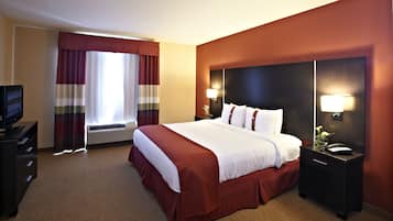 A hotel room with a large bed, a TV, a desk with a lamp, and a window with curtains.