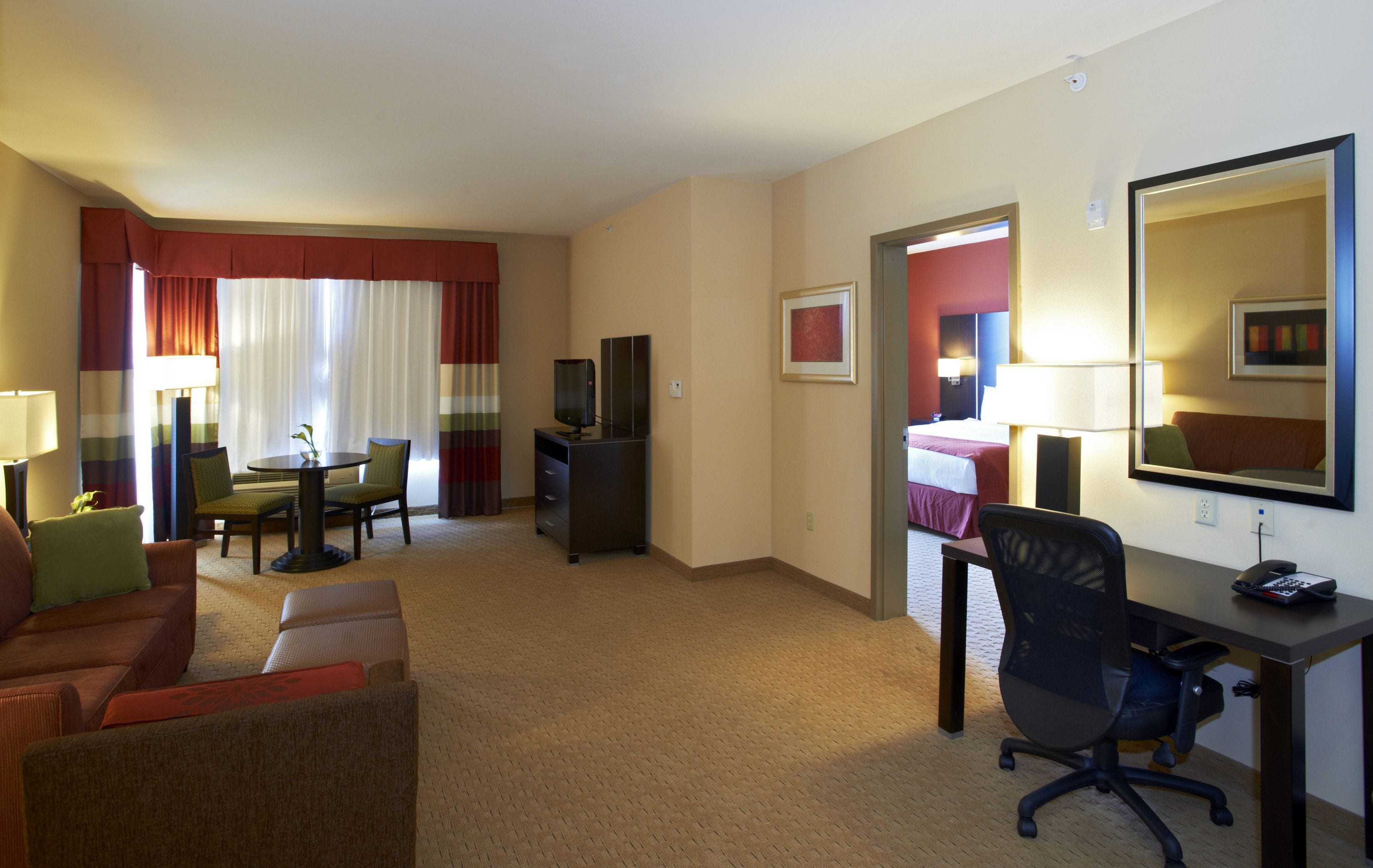 Une chambre d’hôtel comprenant un coin salon, une table à manger, un téléviseur, un bureau et un lit.
