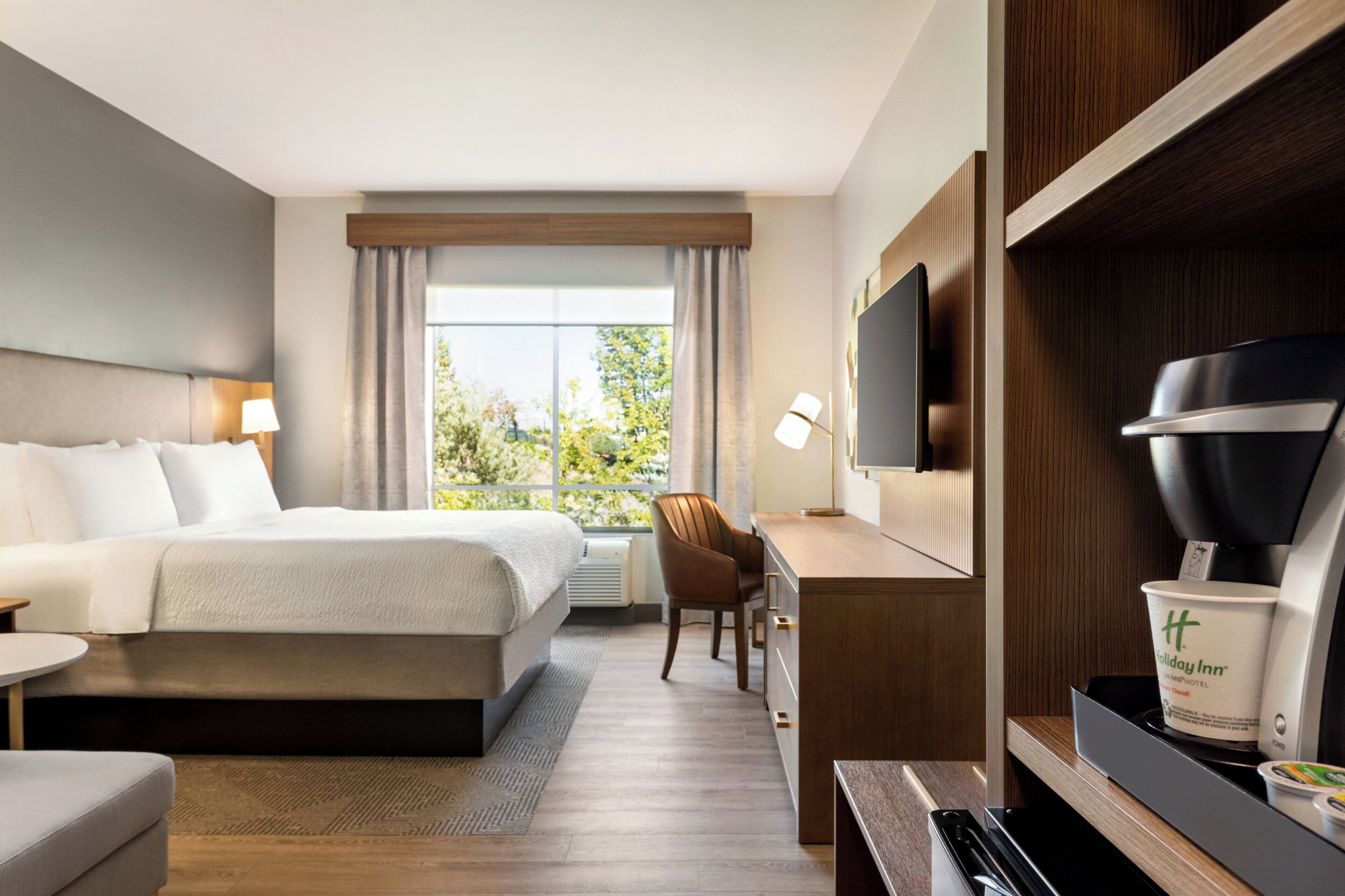 Habitación de hotel con cama, escritorio, silla, televisor y cafetera.