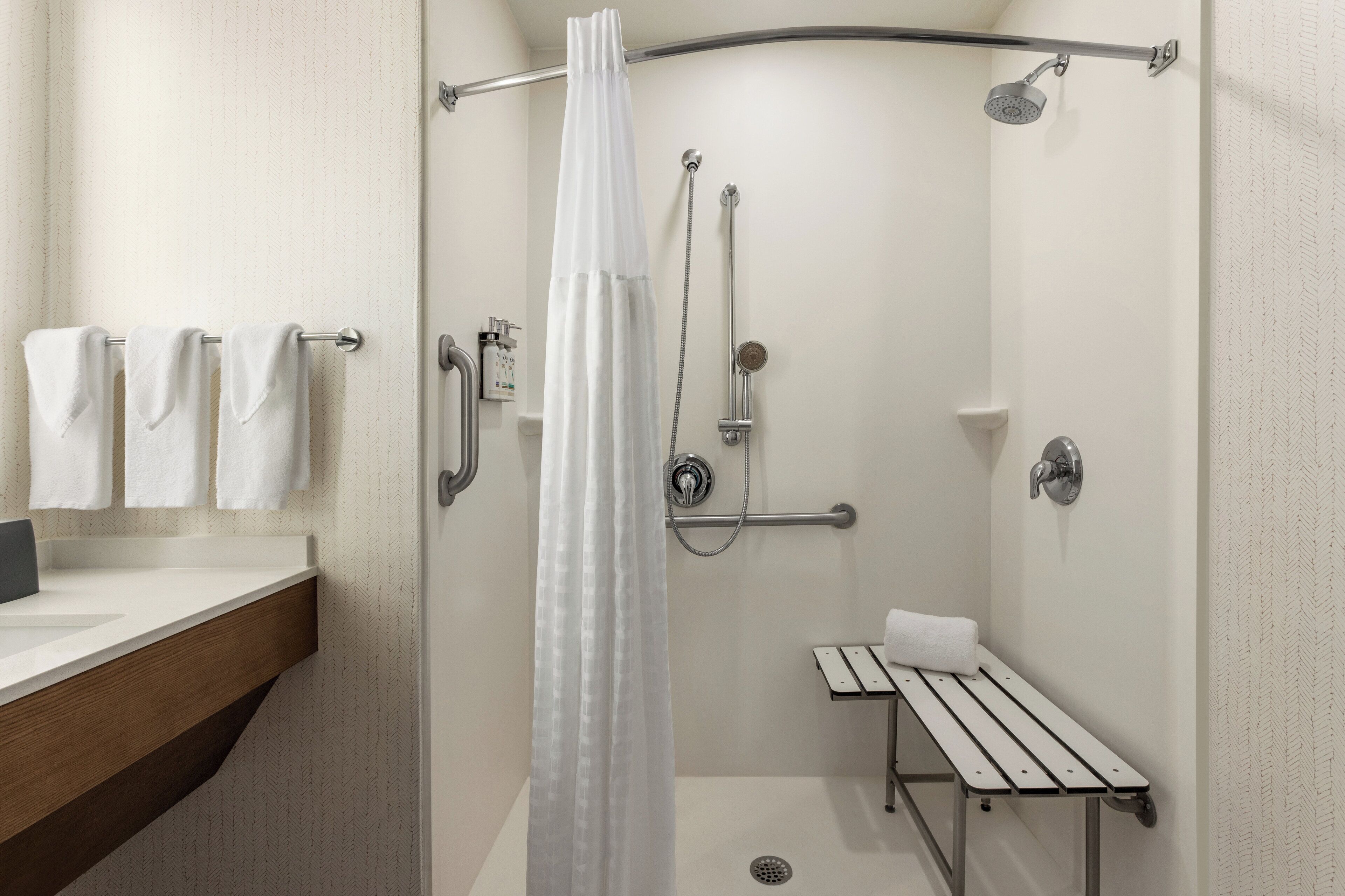 A modern bathroom with a shower, a bench, and a towel rack.