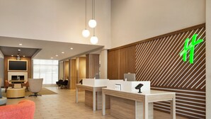 Eine moderne Hotelhalle mit Rezeption, Sitzgelegenheiten und einem großen Bildschirm.