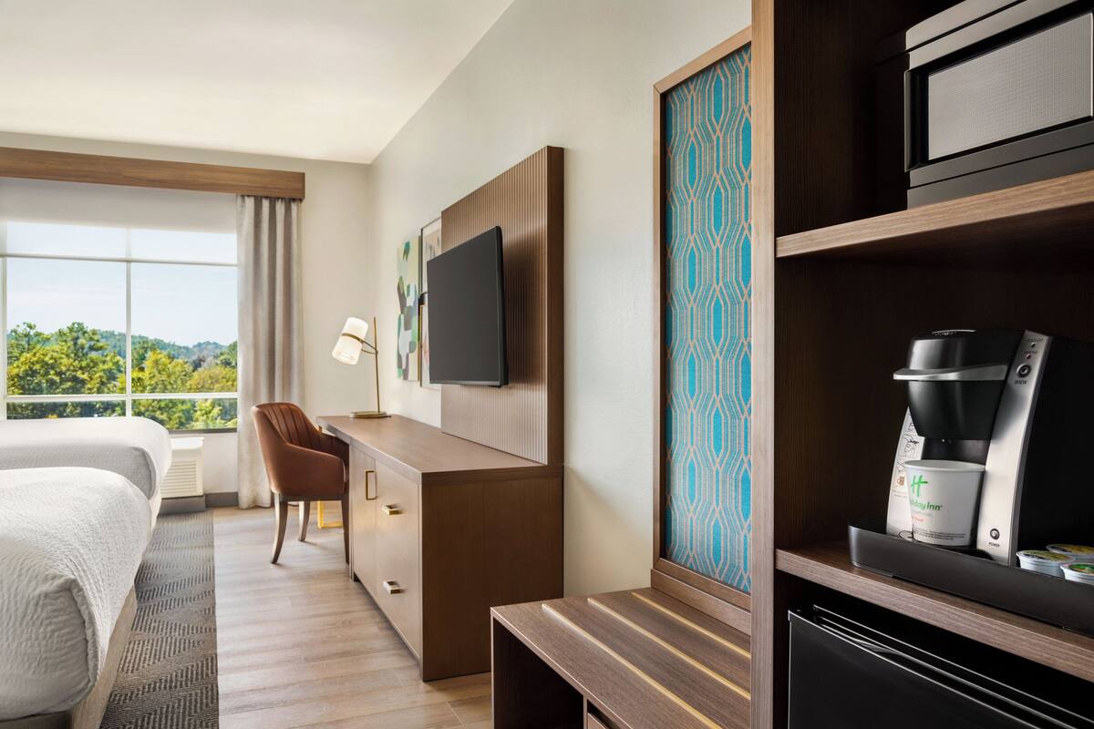 A hotel room with a bed, desk, chair, television, coffee maker, and a view of the outdoors.