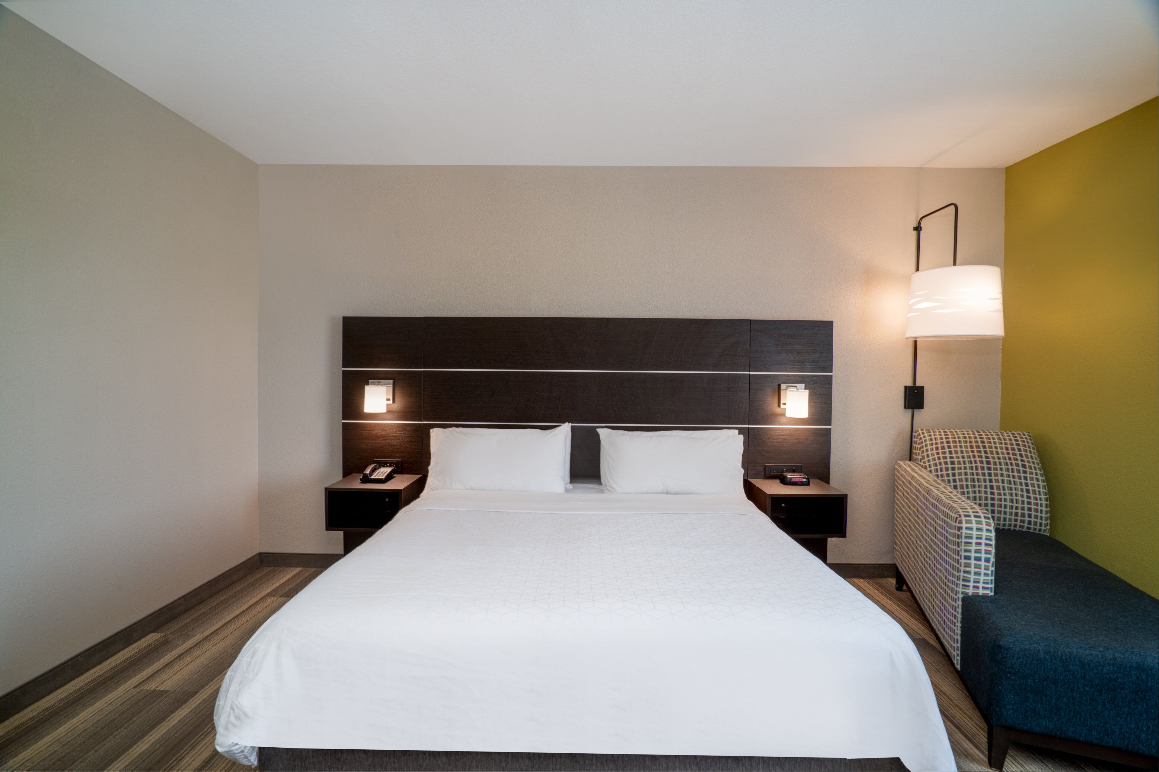 A hotel room with a large bed, two bedside tables, a nightstand, a lamp, and a chair.
