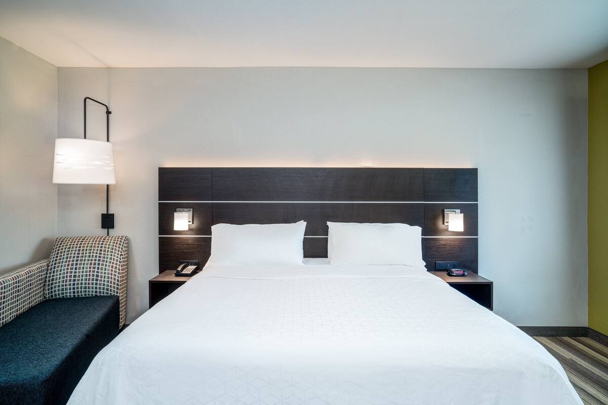 A hotel room with a large bed, two bedside tables, a nightstand, a wall-mounted lamp, and a patterned chair.