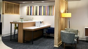 A reception area with a wooden desk, a computer, a lamp, and a colorful striped wall art. - Holiday Inn Express and Suites Winona North by IHG (Winona)