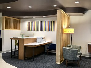 Een receptiegedeelte met een houten toonbank, een computer, een lamp en kleurrijke strepen kunst aan de muur.