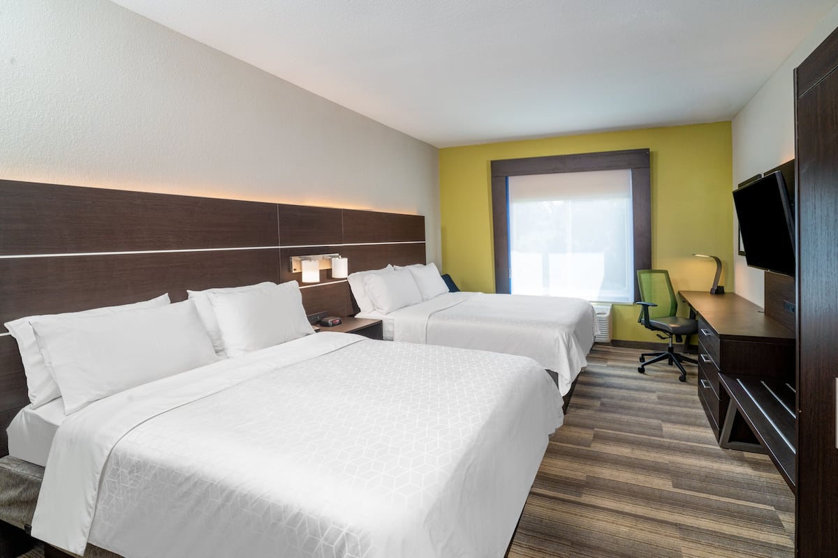 A hotel room with two beds, a desk, a chair, a TV, and a window.