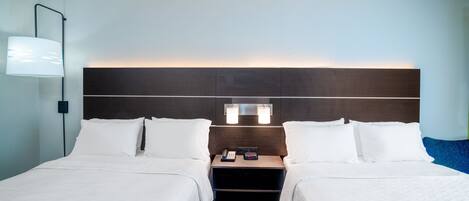 A hotel room with two beds, a nightstand, a lamp, and a wall-mounted light fixture.