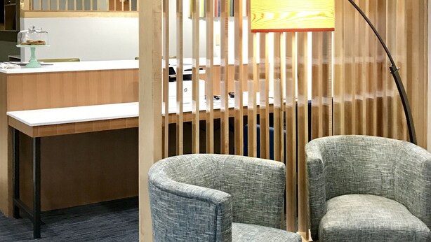 A reception area with a wooden partition, two grey upholstered chairs, a desk with a lamp, and a mirror above the counter. - Holiday Inn Express and Suites Winona North by IHG (Winona)