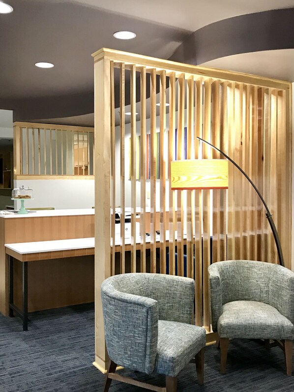 A reception area with a wooden partition, two grey upholstered chairs, a desk with a lamp, and a mirror above the counter. - Holiday Inn Express and Suites Winona North by IHG (Winona)