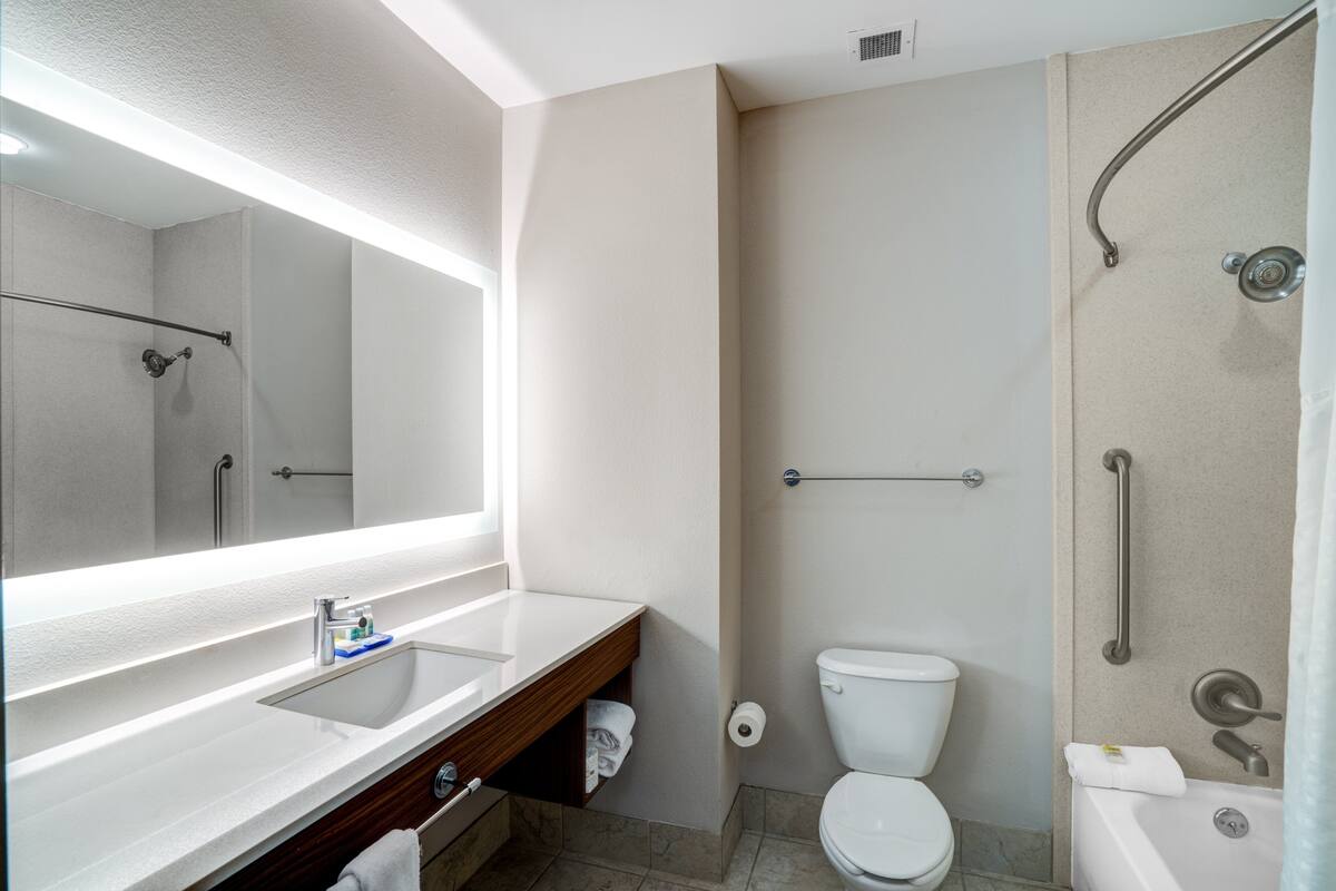 A modern bathroom with a large mirror, a sink, a toilet, and a shower area.