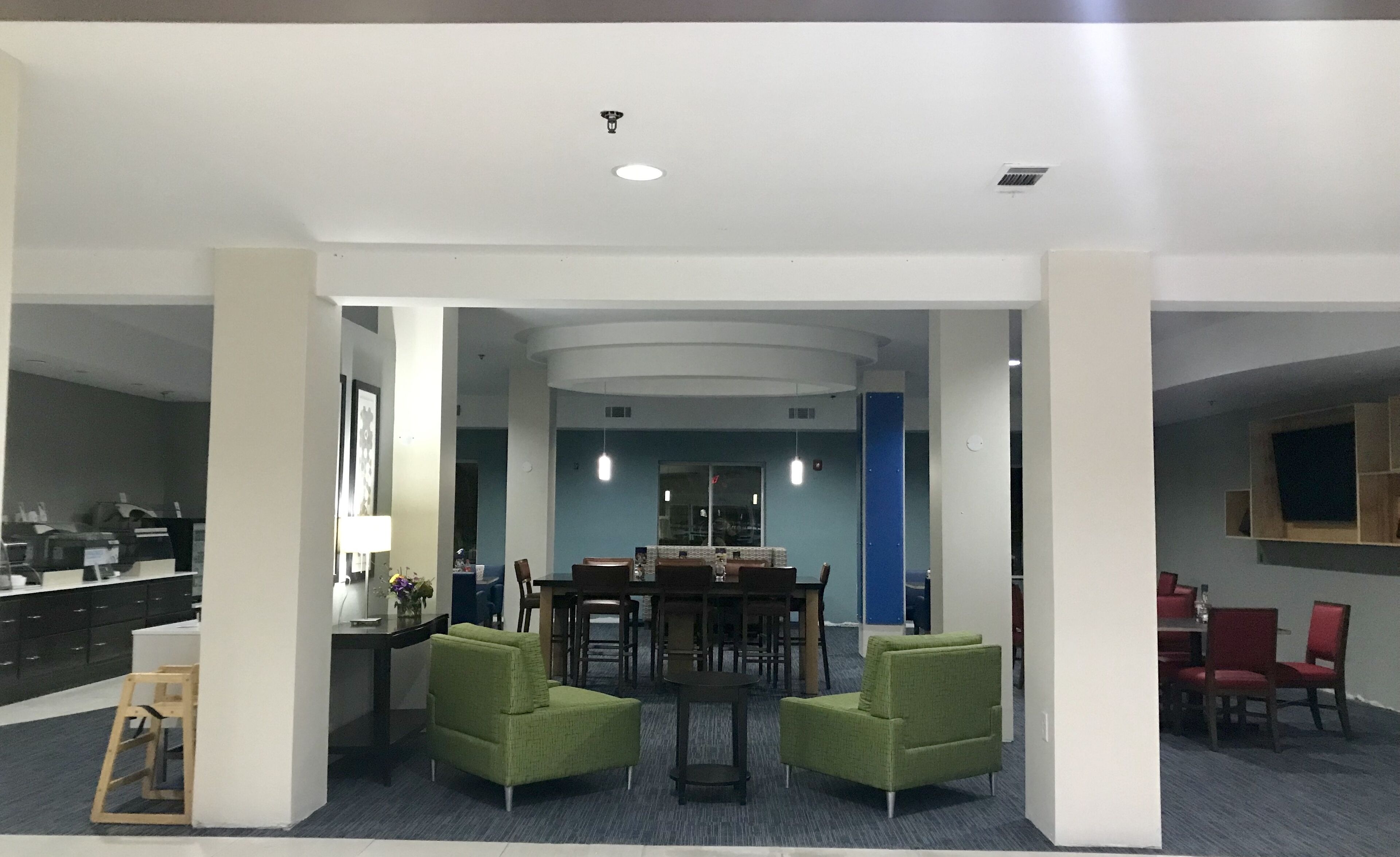 A spacious lobby with a central dining area, green armchairs, and a modern ceiling design.