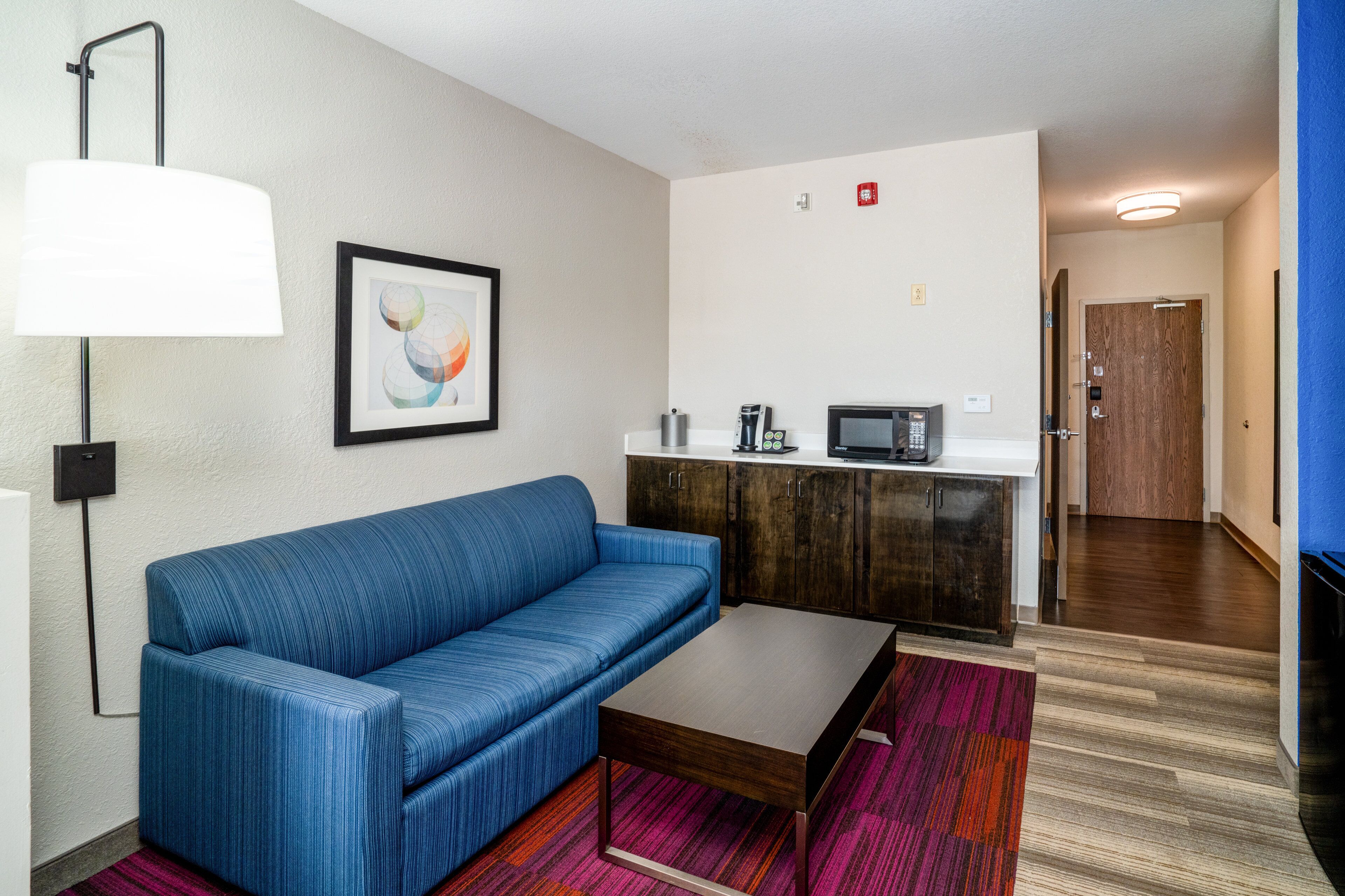 A compact living space with a blue sofa, a coffee table, a microwave, and a small kitchenette.