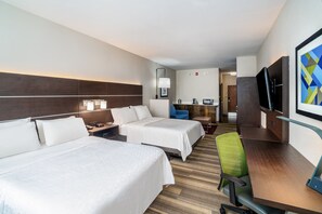 Een hotelkamer met twee bedden, een bureau, een stoel, een televisie en een kitchenette.