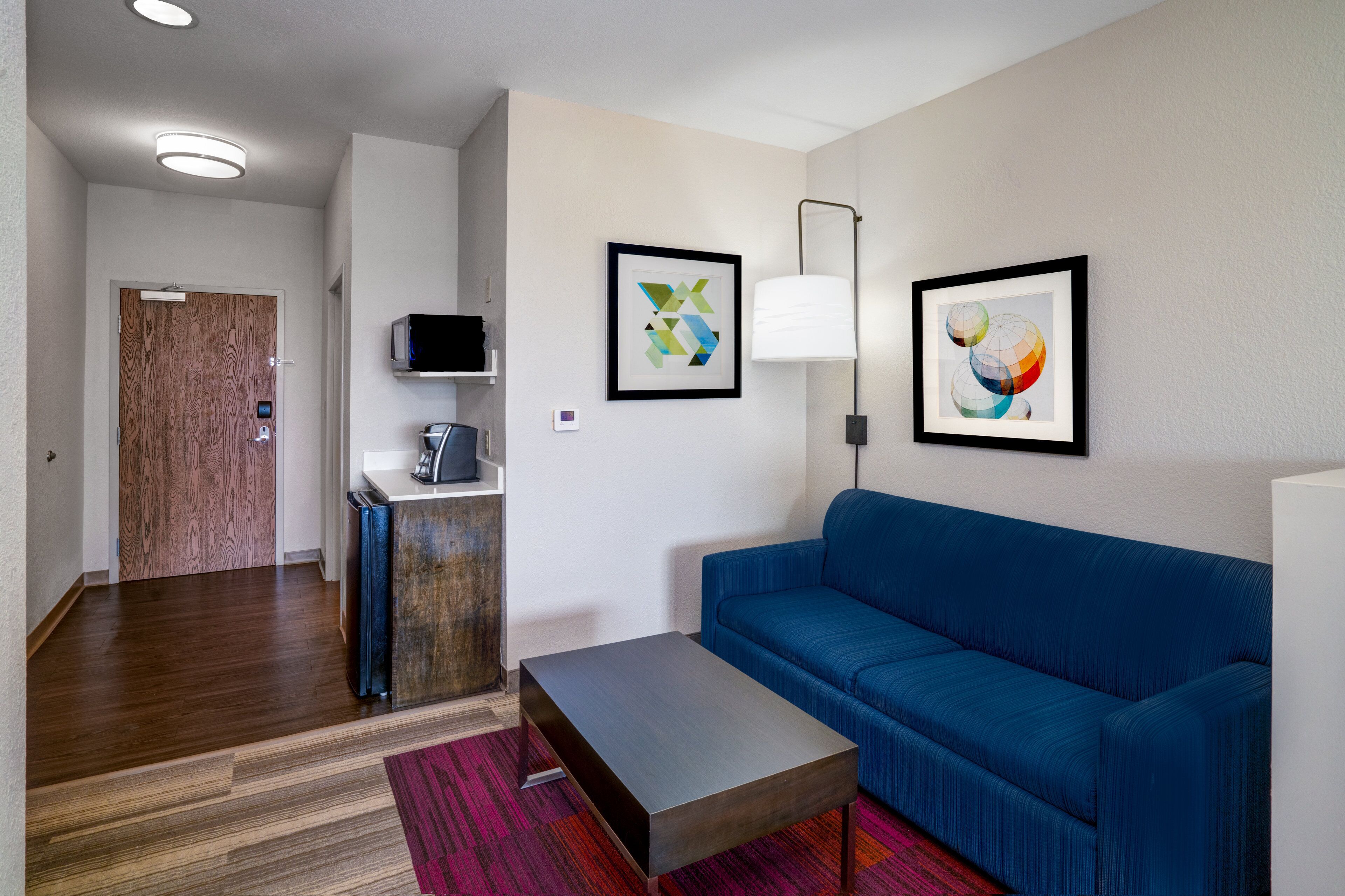 Une chambre d  ’hôtel moderne avec un canapé bleu, une petite table, un four à micro-ondes et une porte en bois.