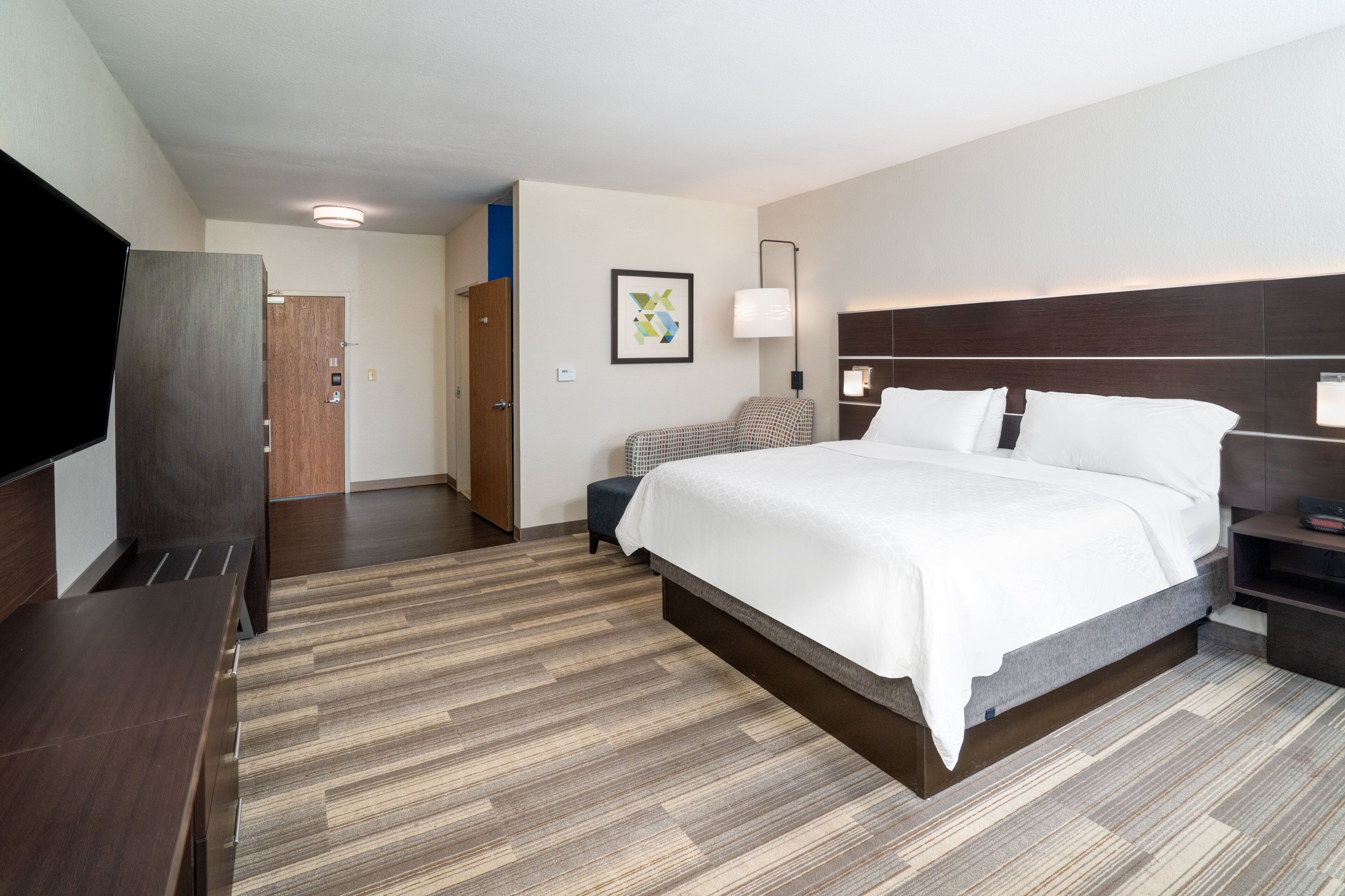 A hotel room with a large bed, a desk, a TV, and a door leading to a bathroom.
