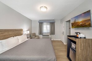 A hotel room with a large bed, a desk with a coffee maker, a TV, and a painting on the wall. - Rodeway Inn Stockton Highway 99 (Stockton)