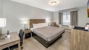 A hotel room with a bed, desk, chair, bedside tables, and a window with curtains. - Rodeway Inn Stockton Highway 99 (Stockton)