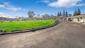 A motel with a parking lot, a grassy area, and a row of buildings. - Rodeway Inn Stockton Highway 99 (Stockton)