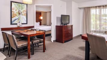 A hotel room with a dining area, a television, a bed, and a window with curtains.