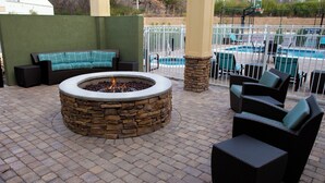 A fire pit surrounded by stone, with outdoor furniture and a pool in the background. - Residence Inn Florence Marriott (Florence)