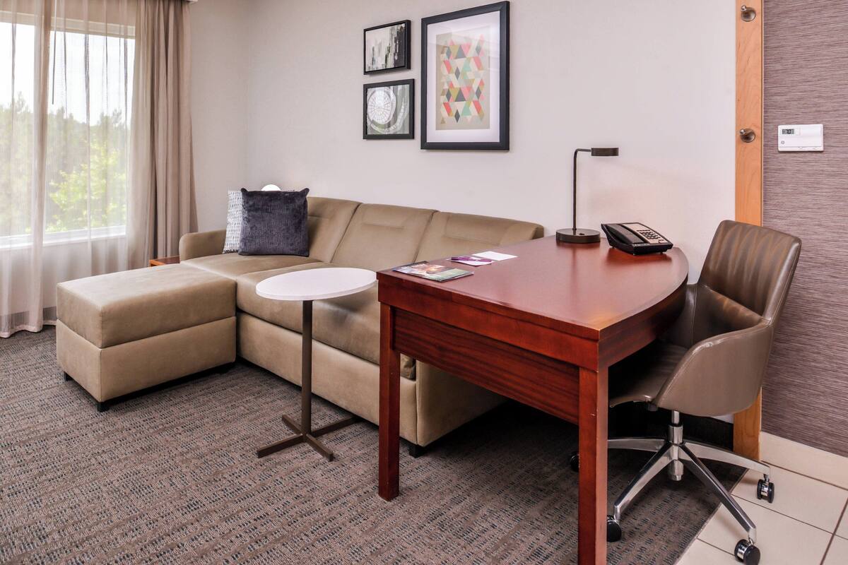 A modern hotel room with a sofa, a desk, a chair, and a small side table.