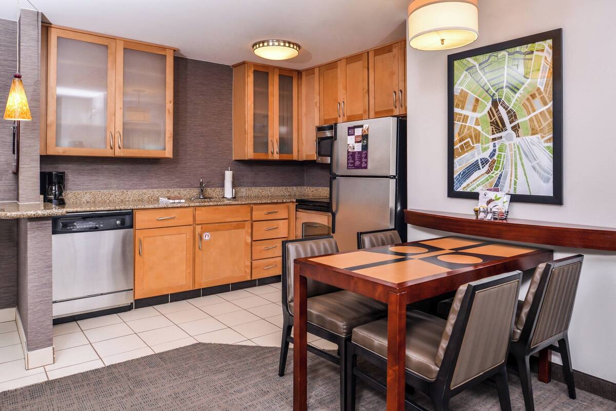 A modern kitchen with wooden cabinets, a stainless steel refrigerator, and a dining table with chairs.
