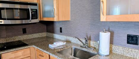A kitchen with wooden cabinets, a stainless steel sink, granite countertops, a microwave, and a paper towel dispenser.