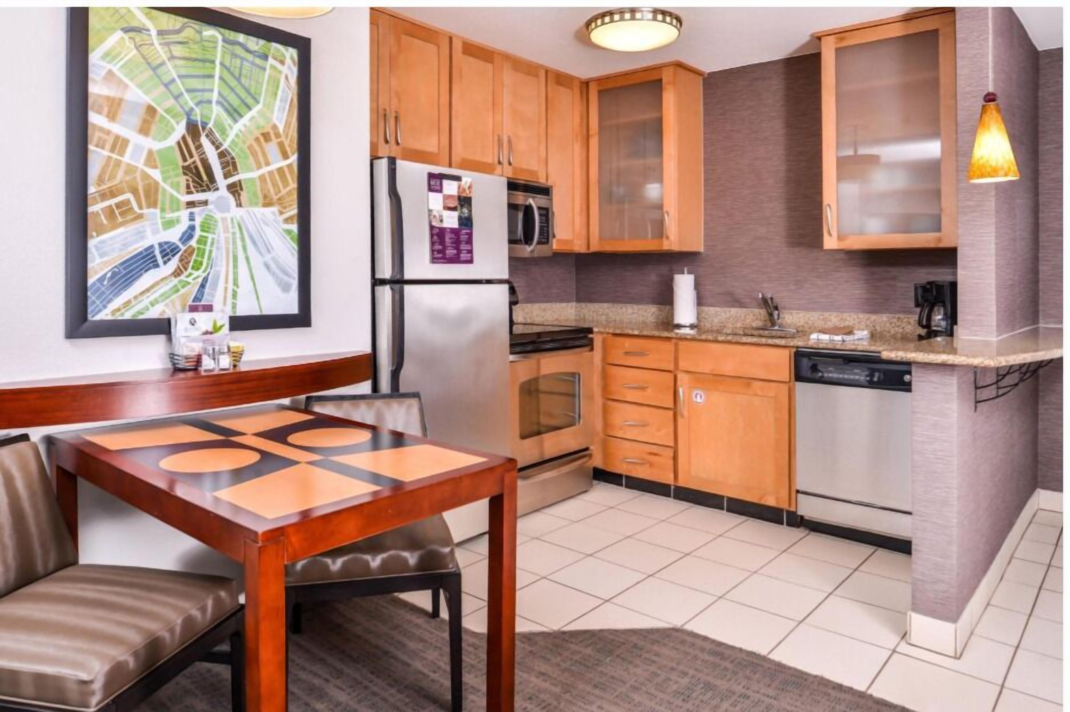 A modern kitchen with wooden cabinets, stainless steel appliances, and a dining area with a table and chairs.
