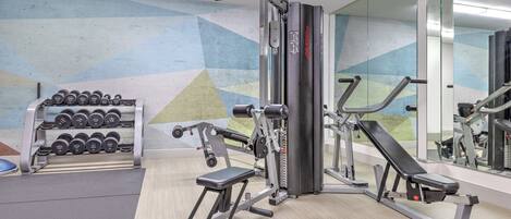 Un gimnasio con máquinas de pesas, mancuernas y una banca.