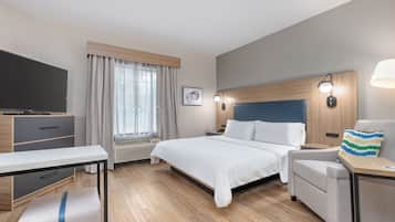 A modern hotel room with a large bed, a desk, a chair, a television, and a window with curtains.