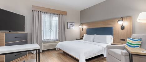A modern hotel room with a large bed, a desk, a chair, a television, and a window with curtains.