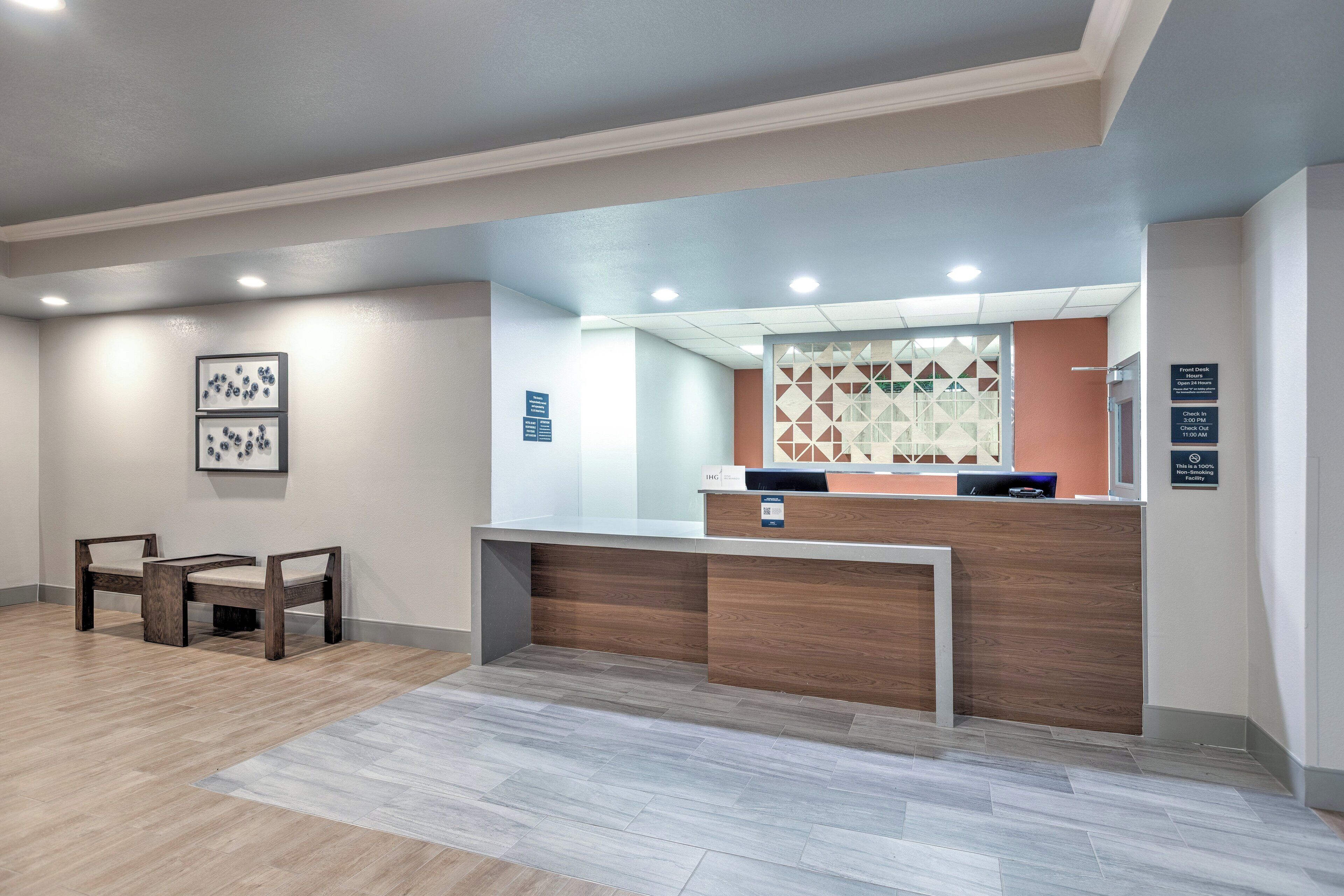 Un espace d’accueil comprenant un comptoir de réception en bois, deux chaises, un mur décoré et un panneau indiquant la réception et le bureau d’accueil.