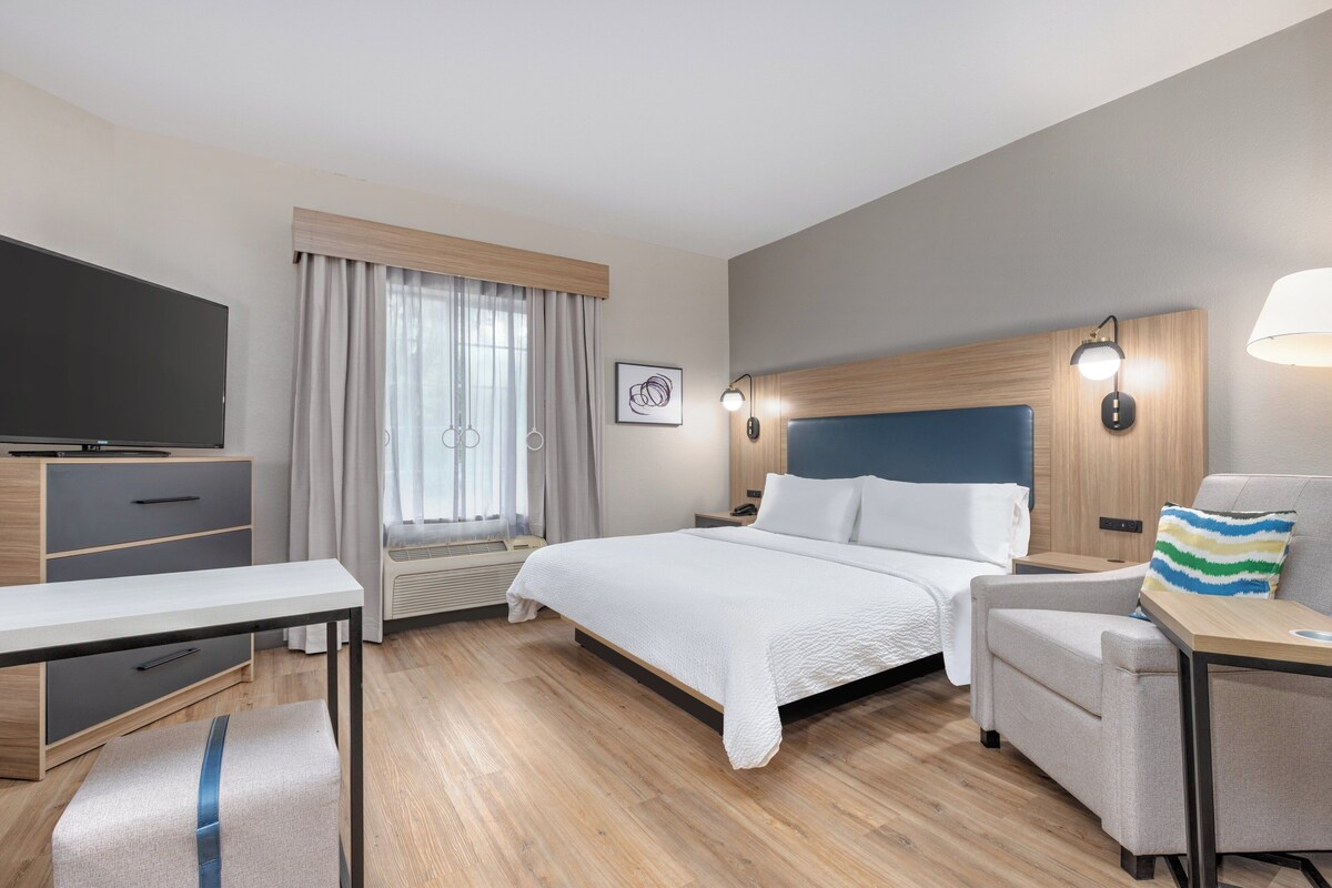 A hotel room with a bed, a desk, a chair, a TV, and a window with curtains.