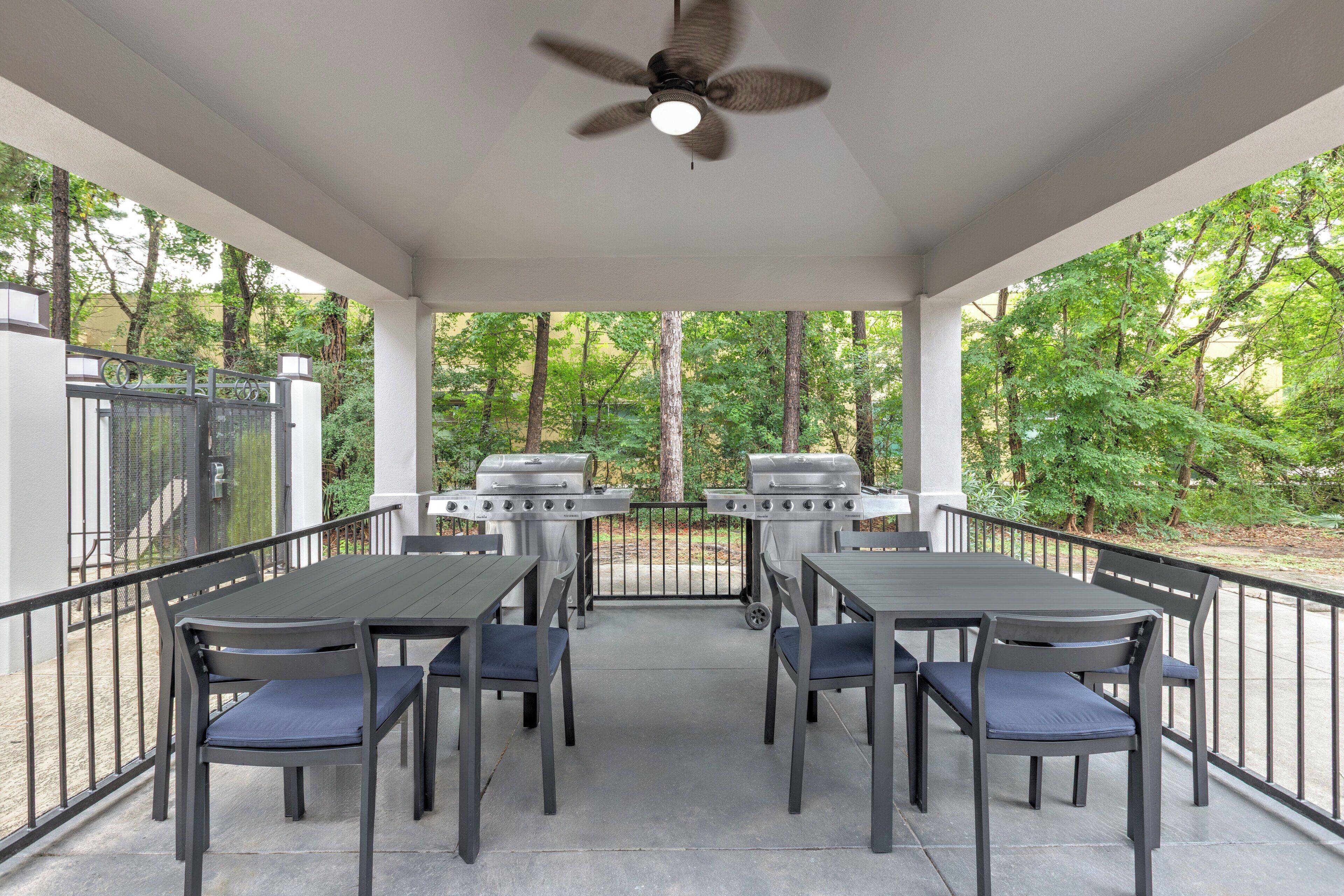 Un patio couvert avec un ventilateur de plafond, deux barbecues et une table avec des chaises.