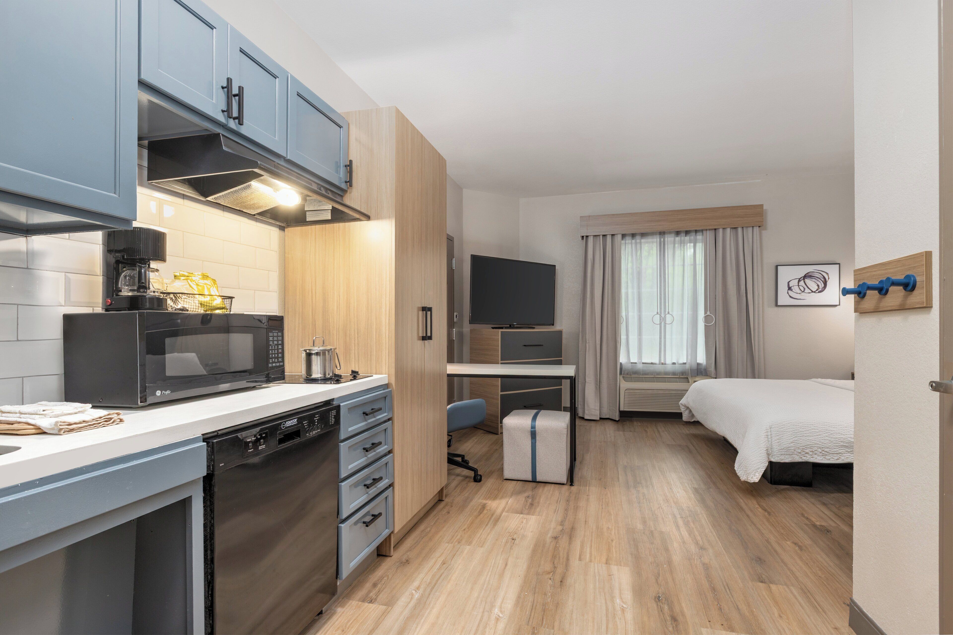 Une chambre d’hôtel de taille réduite, équipée d’une kitchenette, d’un lit, d’un bureau et d’une télévision.