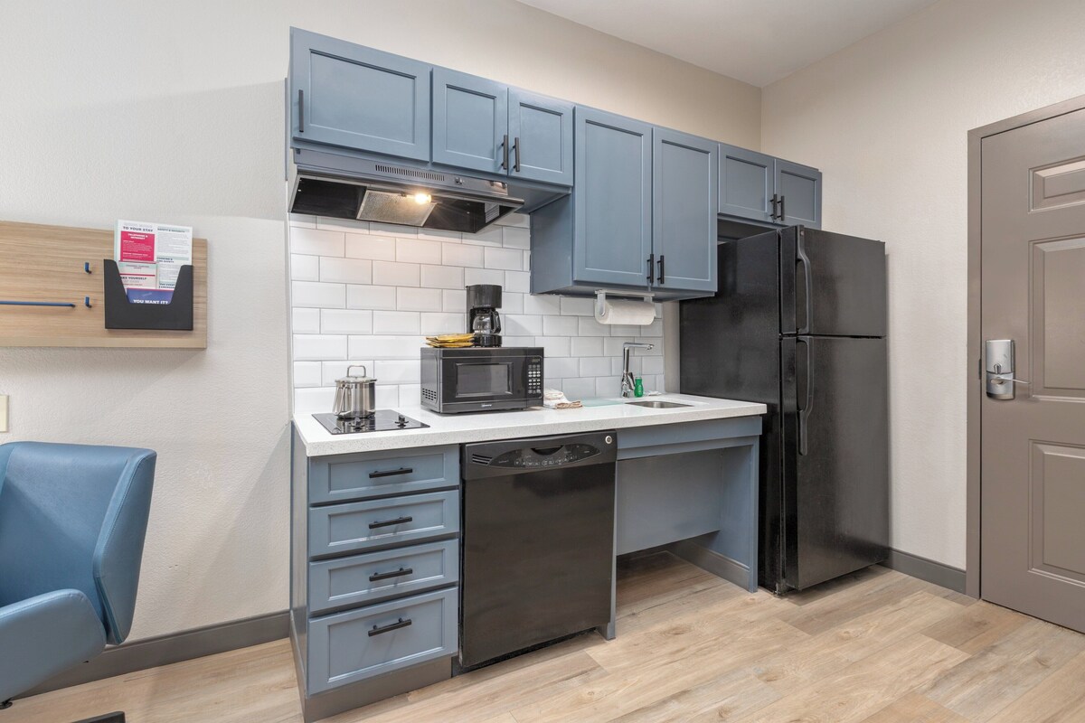 A compact kitchen with grey cabinets, a black refrigerator, a microwave, and a dishwasher.