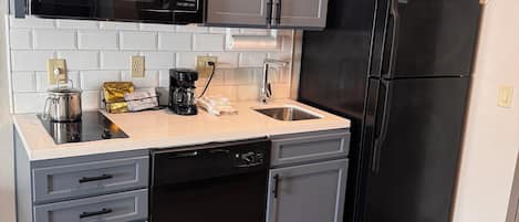 A modern kitchen with grey cabinets, a black refrigerator, a microwave, and a dishwasher.