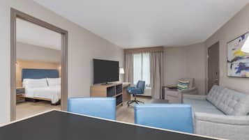 A hotel room with a bed, a desk with a chair, a sofa, a TV, and a painting on the wall.