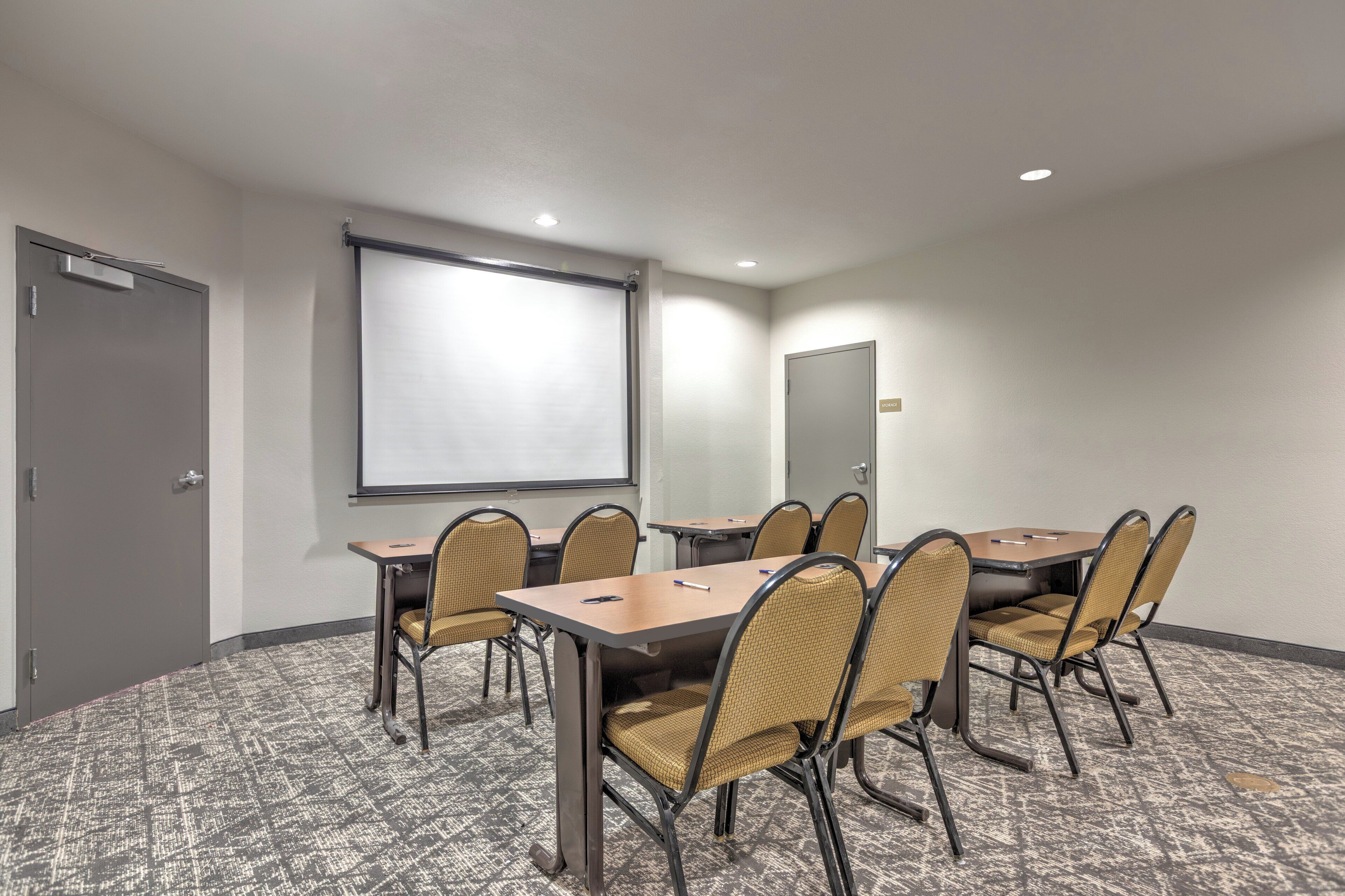 A conference room with a large screen, a round table, and six chairs.