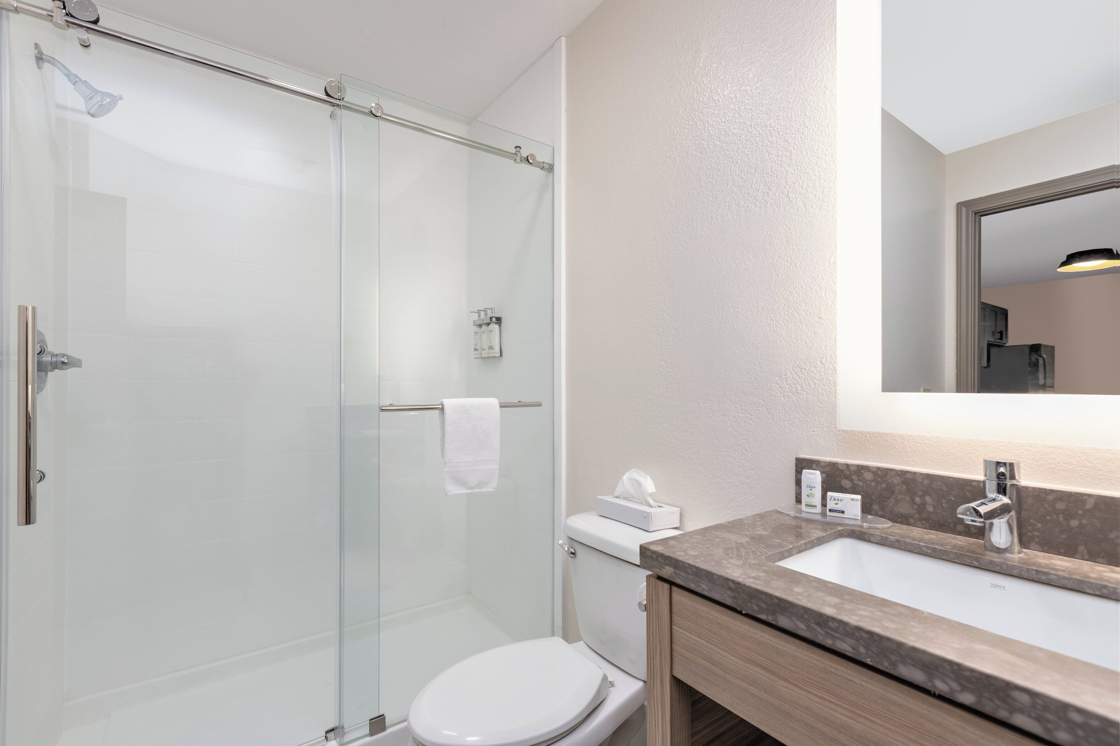 Une salle de bain moderne avec une douche à parois de verre, des toilettes blanches et un lavabo en marbre avec un miroir au-dessus.
