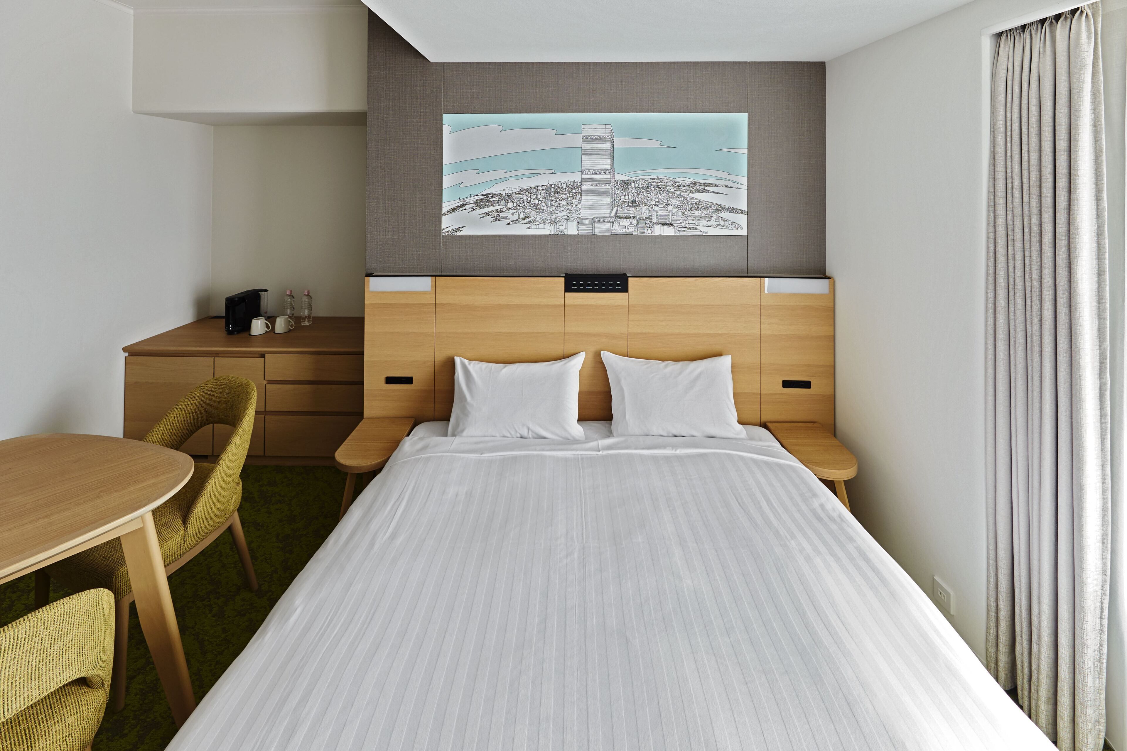 A hotel room with a large bed, a wooden desk, a chair, and a painting of a cityscape on the wall.