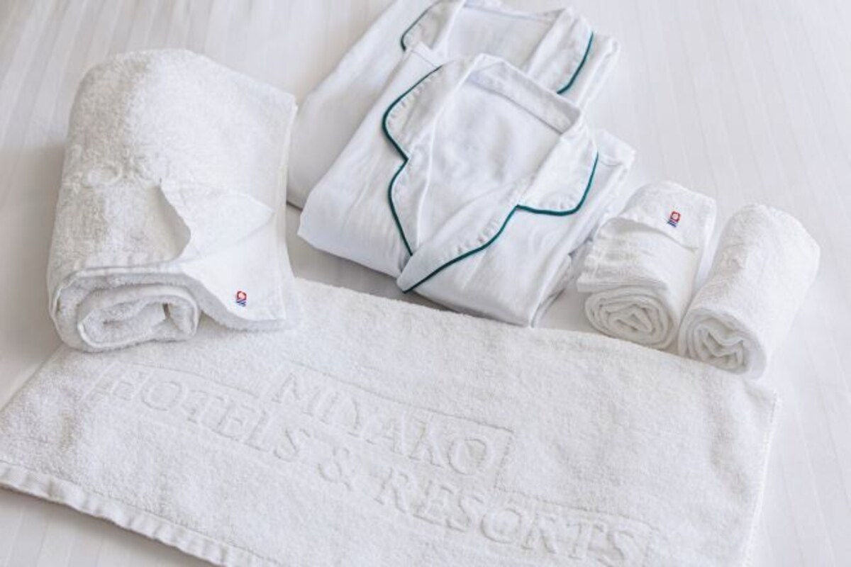 Neatly folded white towels and robes with green piping, and a towel with "MIYAKO HOTELS & RESORTS" embossed on it.